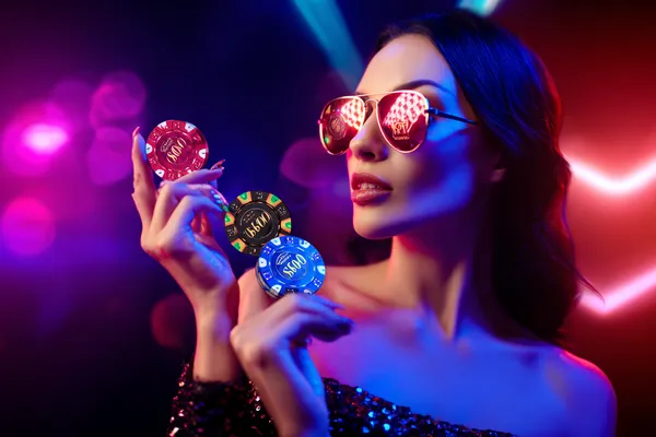 A woman smiling while playing online games on her laptop, surrounded by neon casino elements, showcasing TALABAT’s diverse game collection.